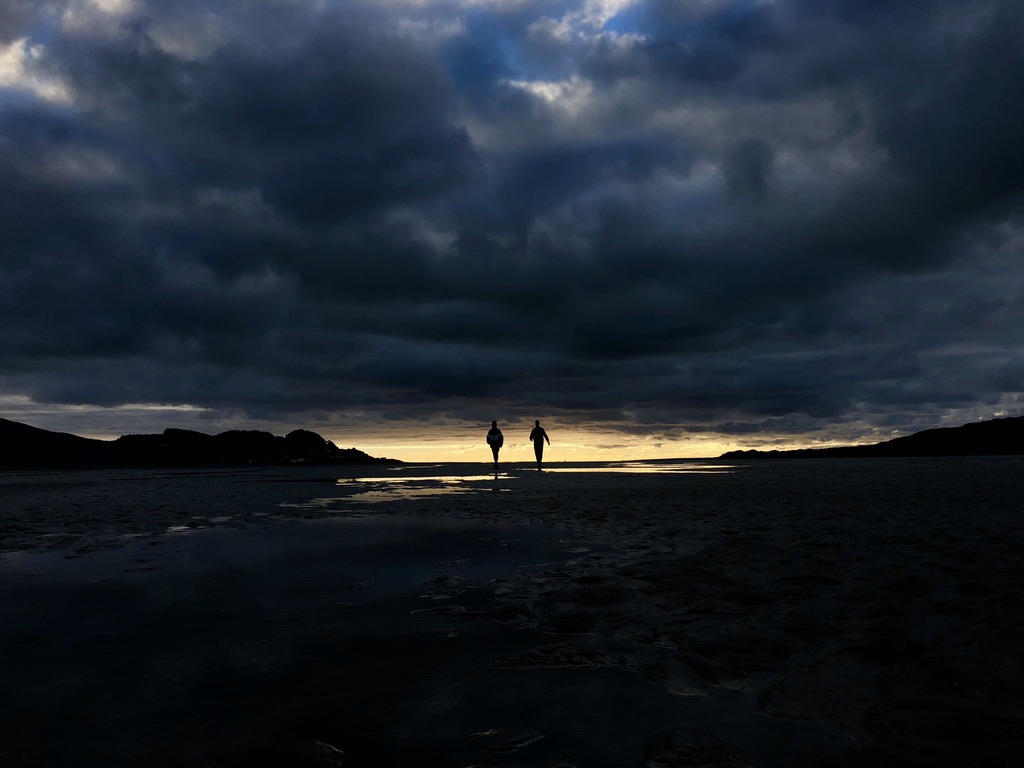 Two silhouettes walking against a dramatic sunset sky