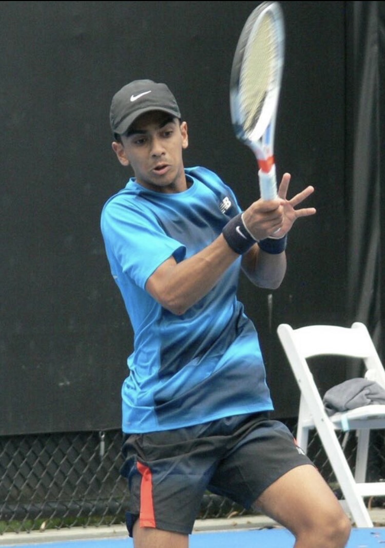 Action shot of Rahul playing tennis, hitting a forehand in a blue Nike shirt